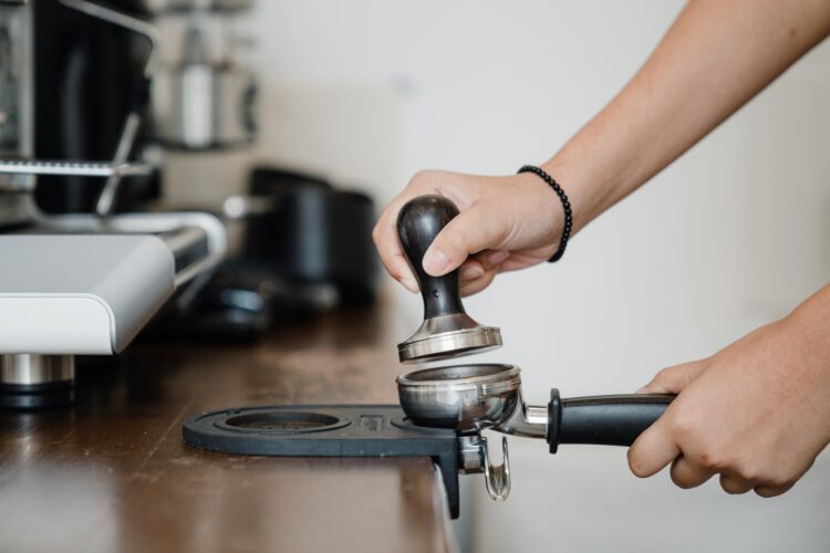 crop barista pressing coffee beans with tamper